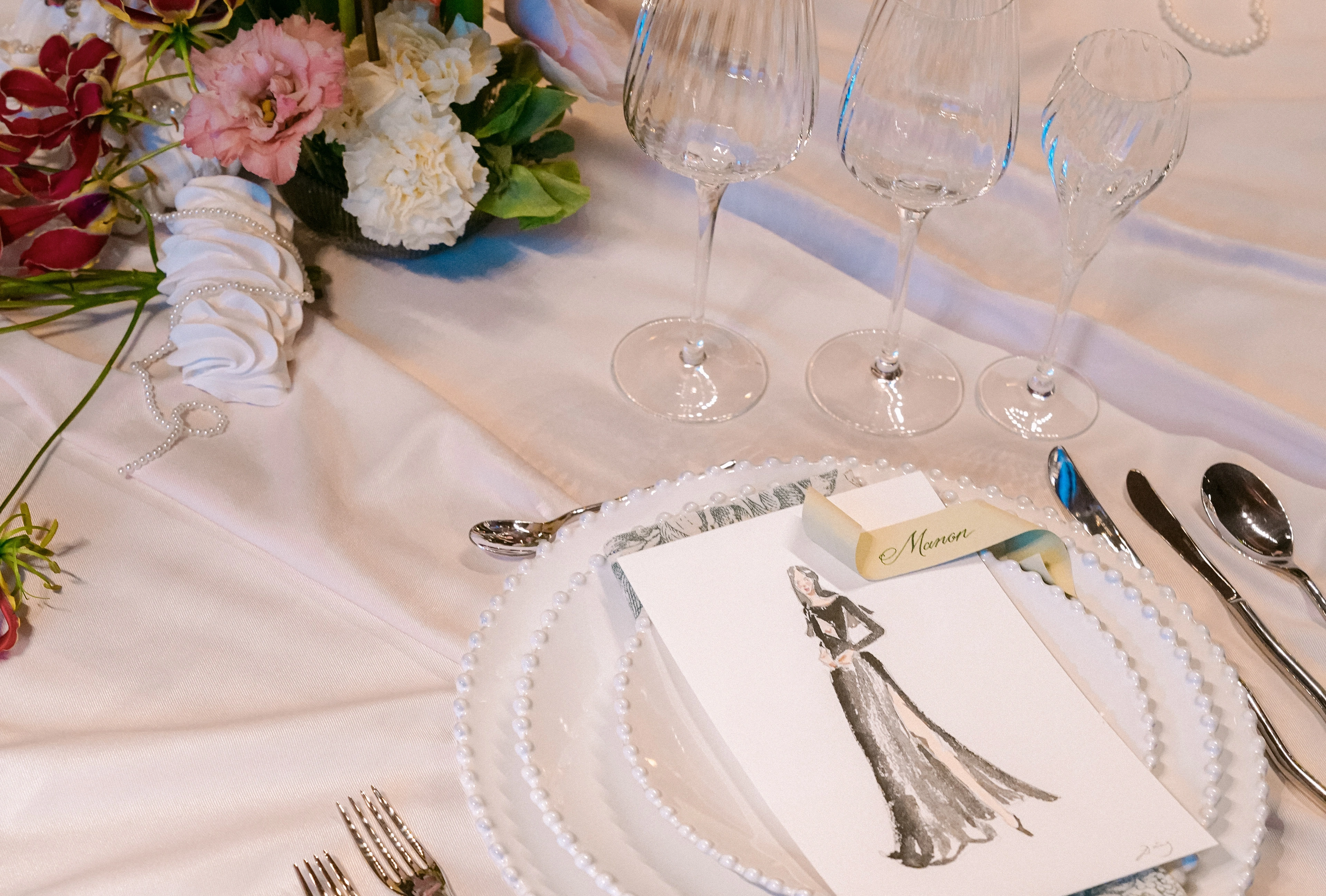 Watercolor guest portrait used as a place card on a wedding table at InterContinental Geneva, beside crystal glasses and flowers. © Laura's Creativity