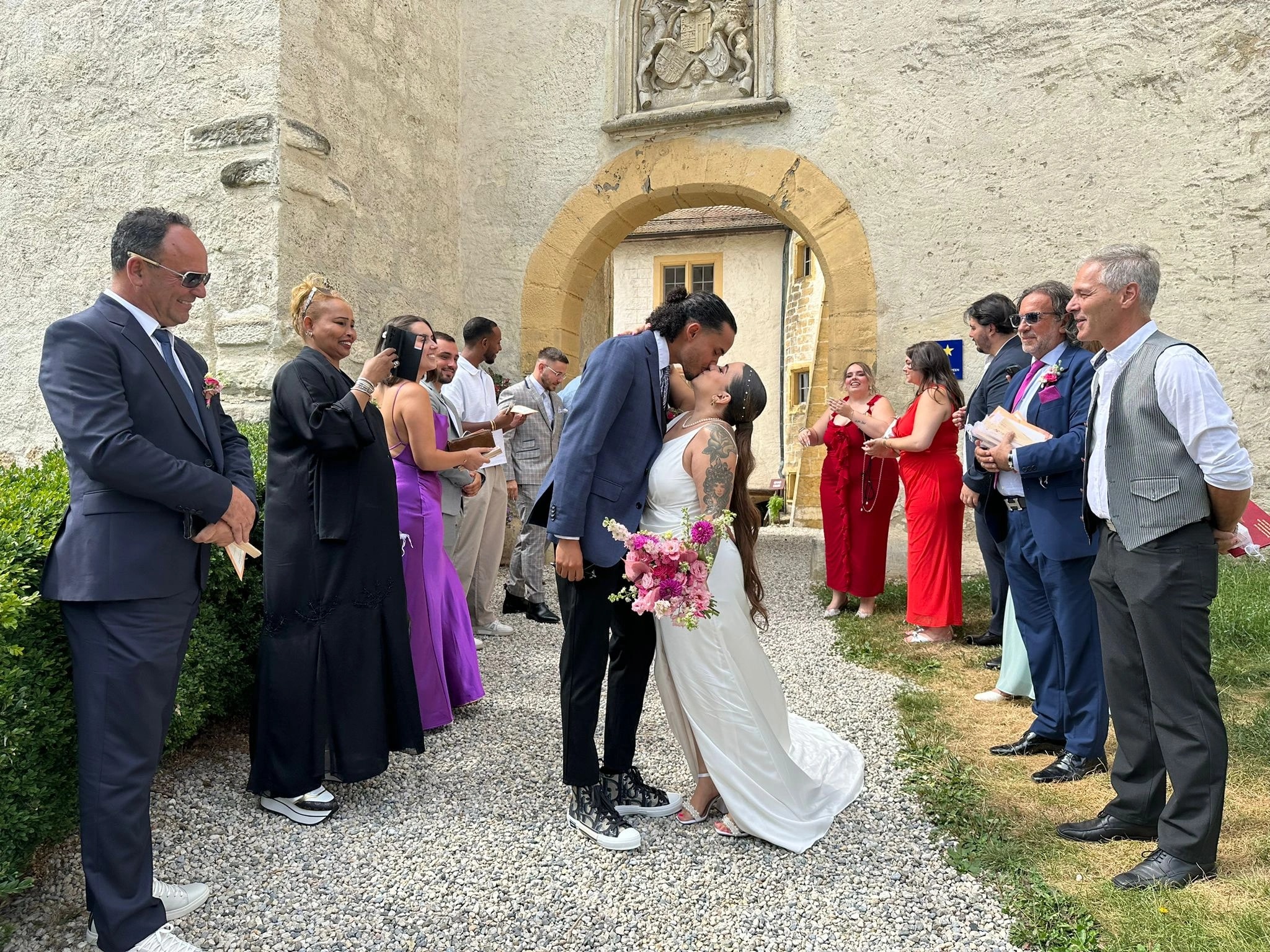 Brautpaar küsst sich im Hof des Château de La Sarraz unter den Augen der Gäste, Referenzfoto für die Live-Hochzeitsmalerei