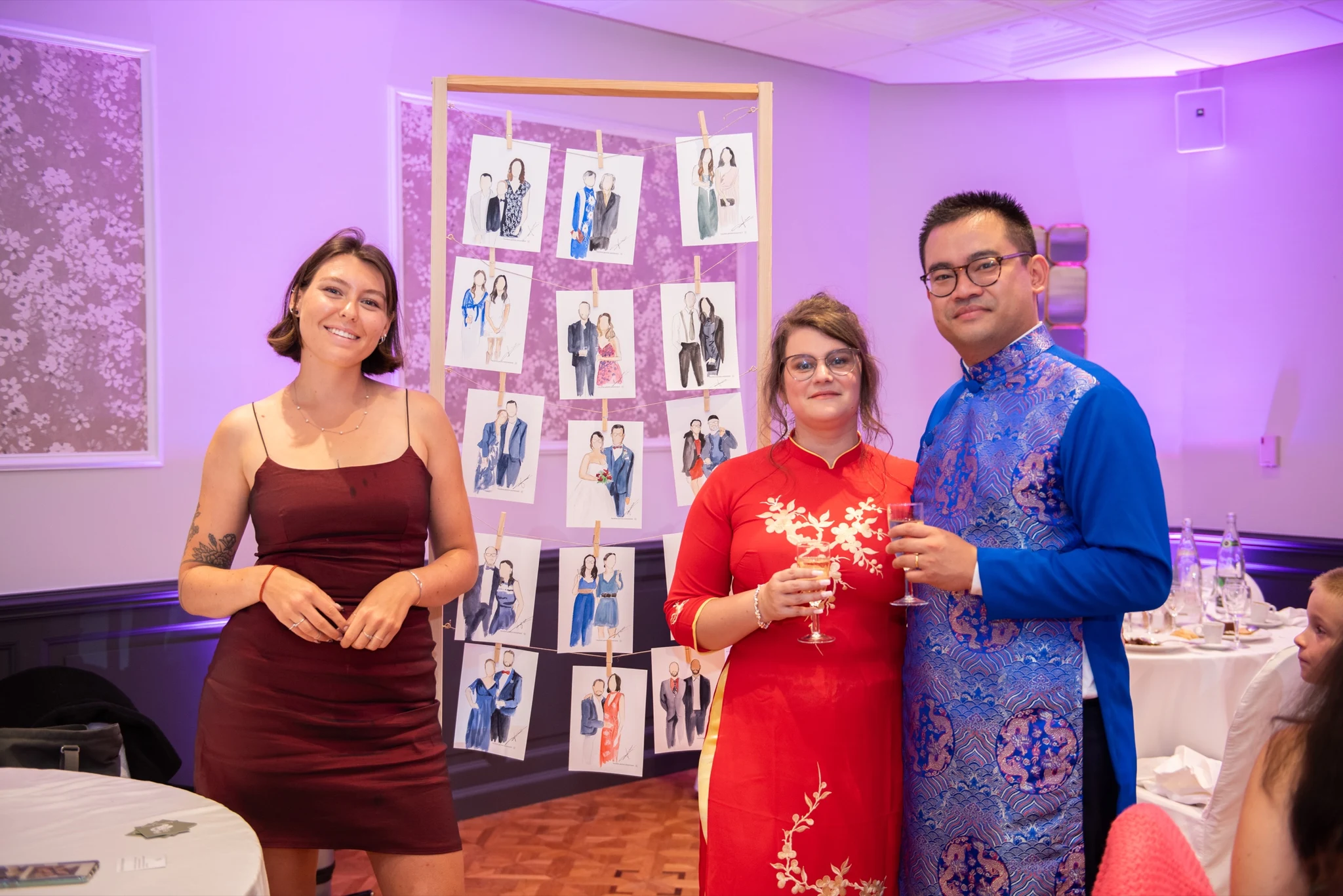 Bride and groom in ao dai in front of the wall of watercolour guest portraits at their wedding in Gouvieux. Photography by GC Photographie.