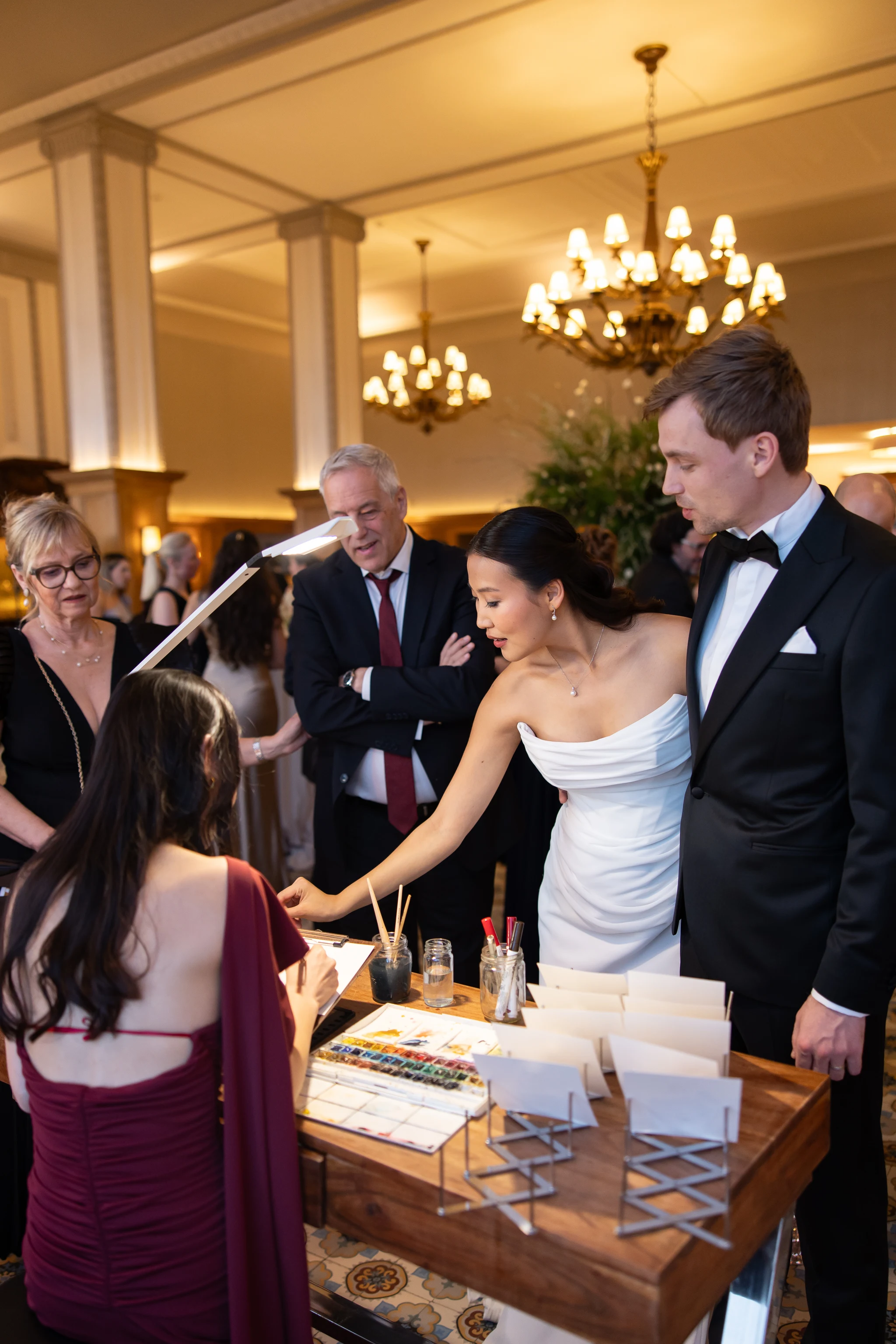 Bride and groom admiring their guests’ watercolor portraits at the painting station, Villars Palace. © LeighAnn