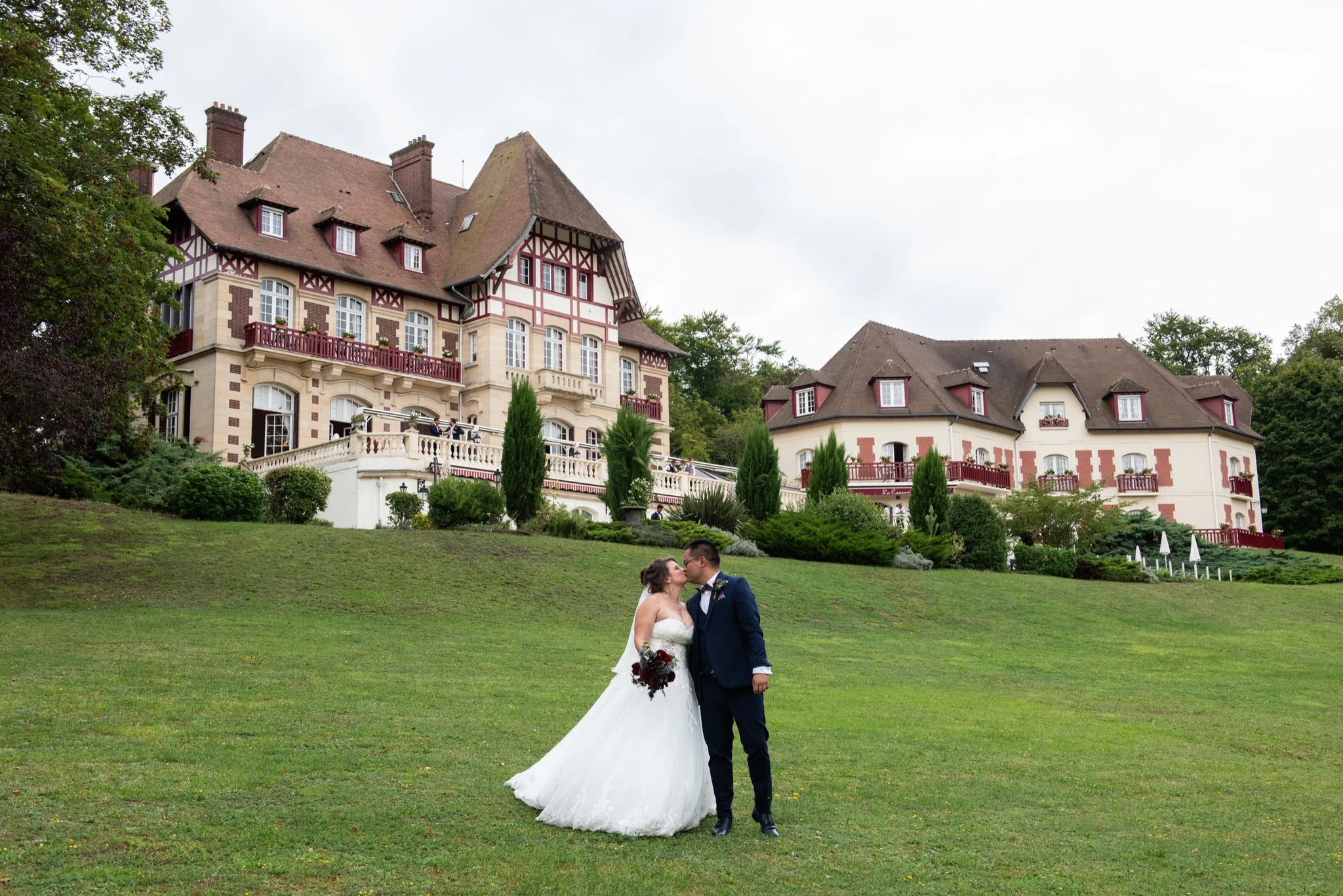 Bride and groom kissing on the lawn in front of Château de la Tour in Gouvieux, France. Photography by GC Photographie.