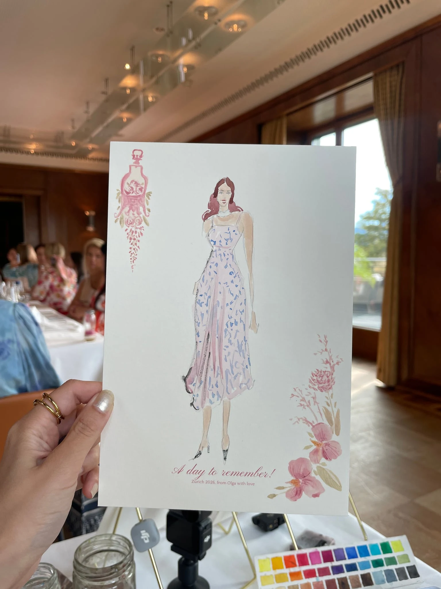 Live watercolor illustration of a guest in a lilac patterned dress at a birthday party at AMERON Zürich Bellerive au Lac.