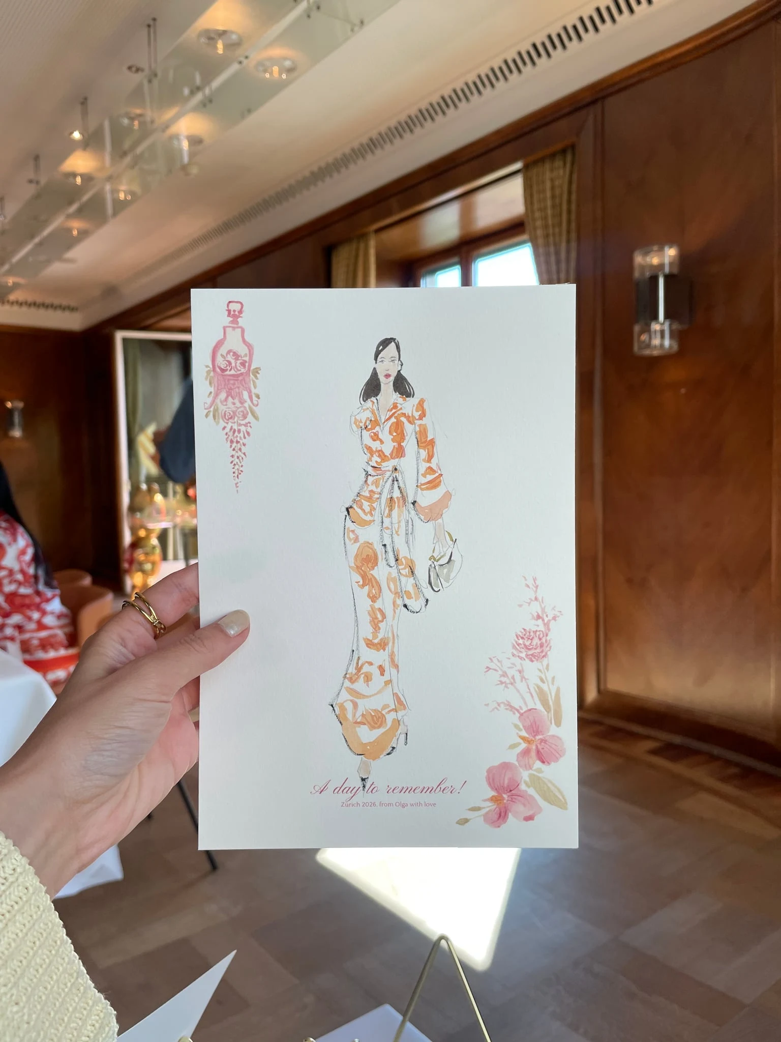 Live watercolor illustration of a guest in an orange floral dress at a birthday party at AMERON Zürich Bellerive au Lac.