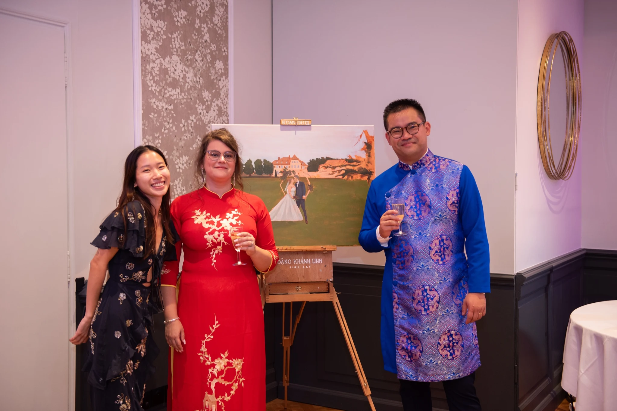 Live wedding painter with the bride and groom in ao dai beside their wedding painting at Château de la Tour, Gouvieux. Photography by GC Photographie.