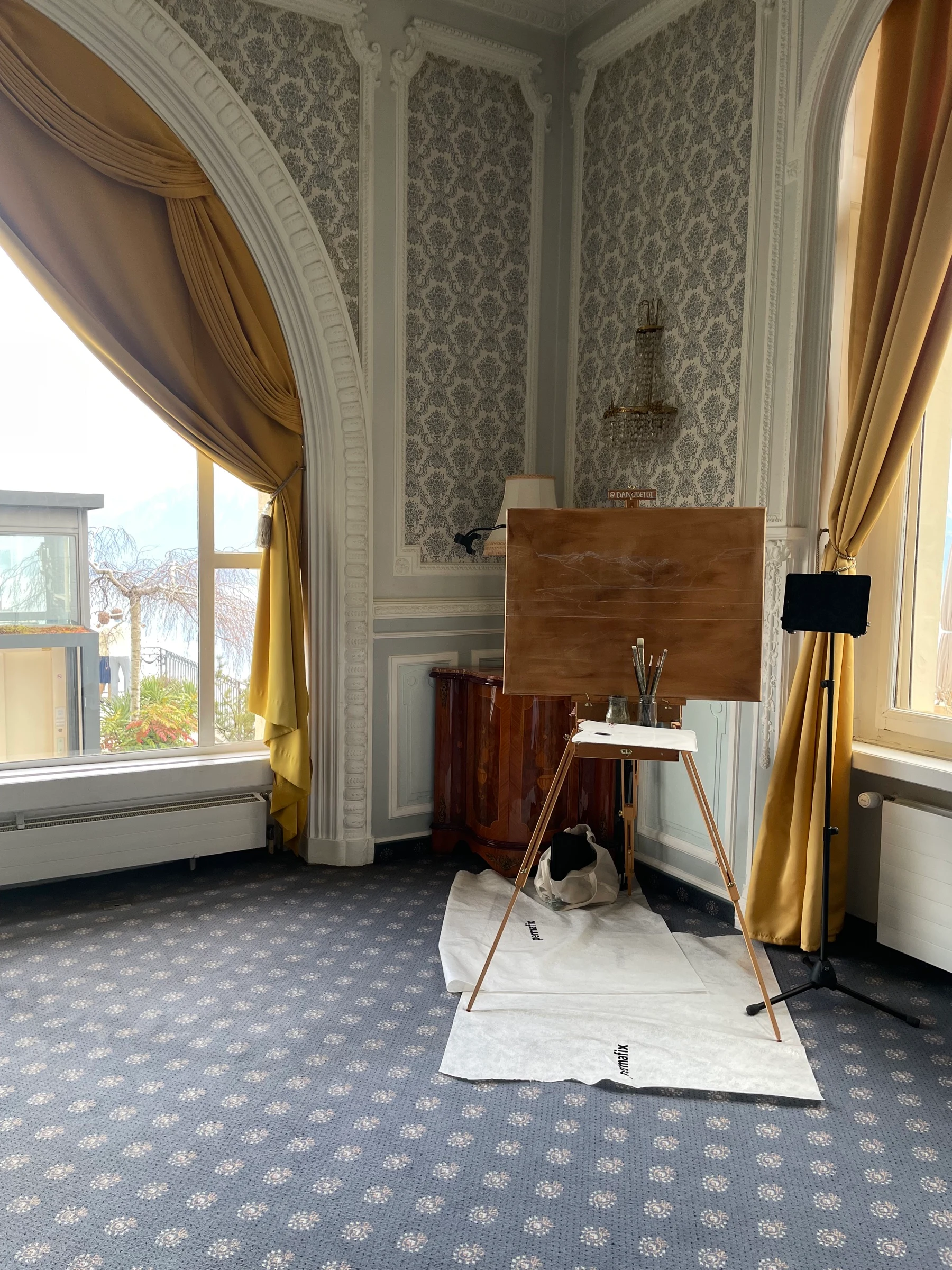 Easel with a blank orange canvas set up in an elegant salon with an arched window and gold curtains at Le Mirador
