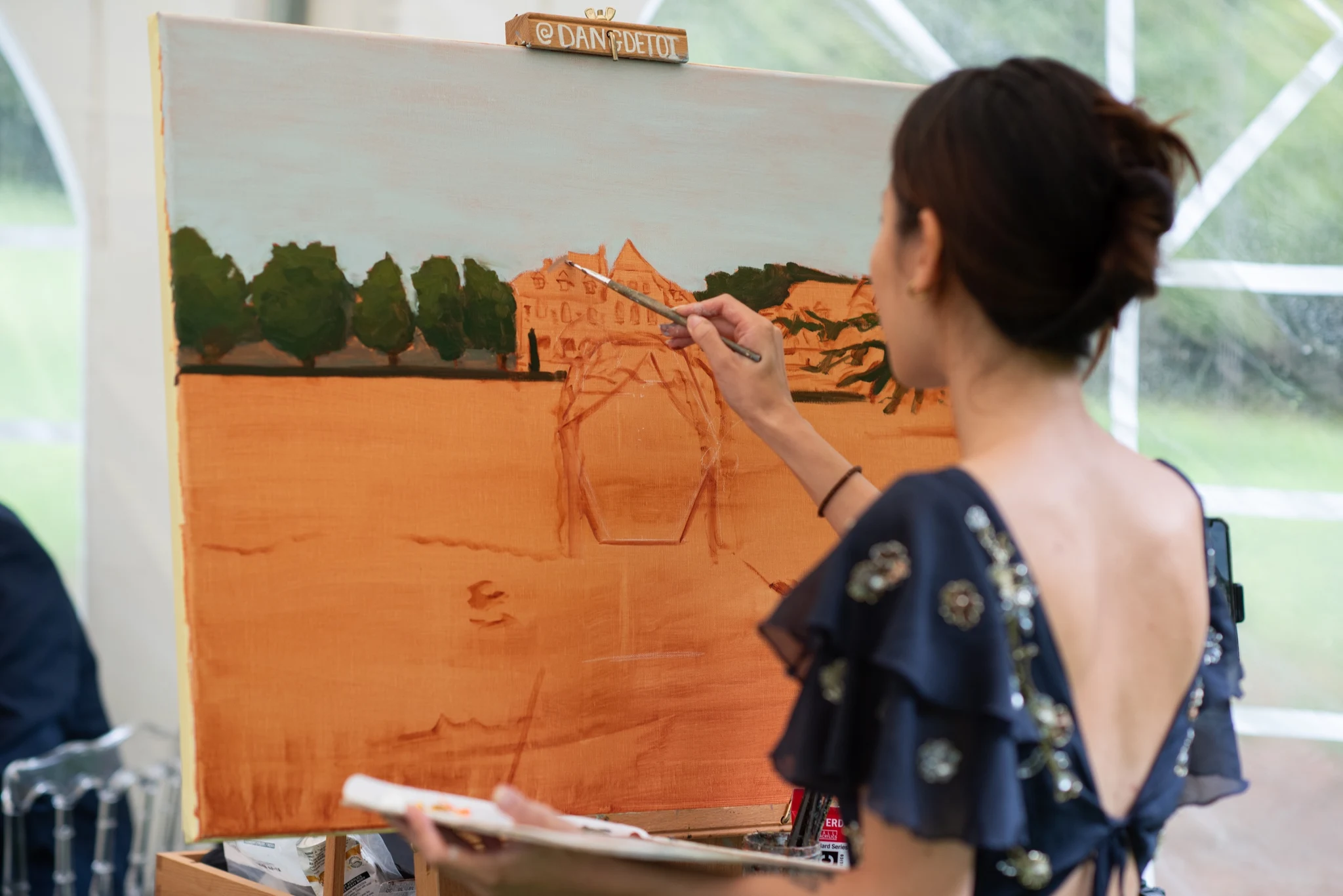 Live wedding painter working on the orange underpainting of Château de la Tour on a canvas. Photography by GC Photographie.