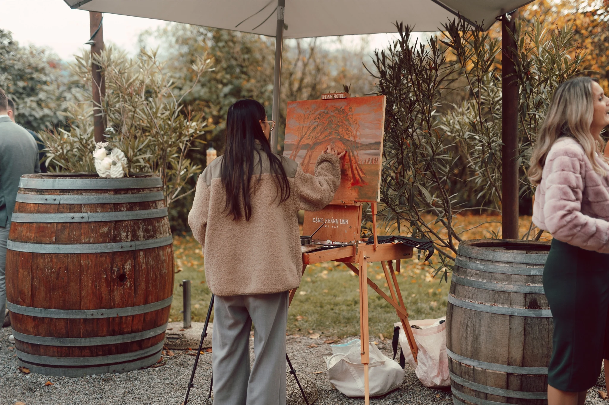 Live wedding painter working at her easel under a parasol between wine barrels at Moschti Stäfa. Photography by Geraldine Rhyner Fotografie.