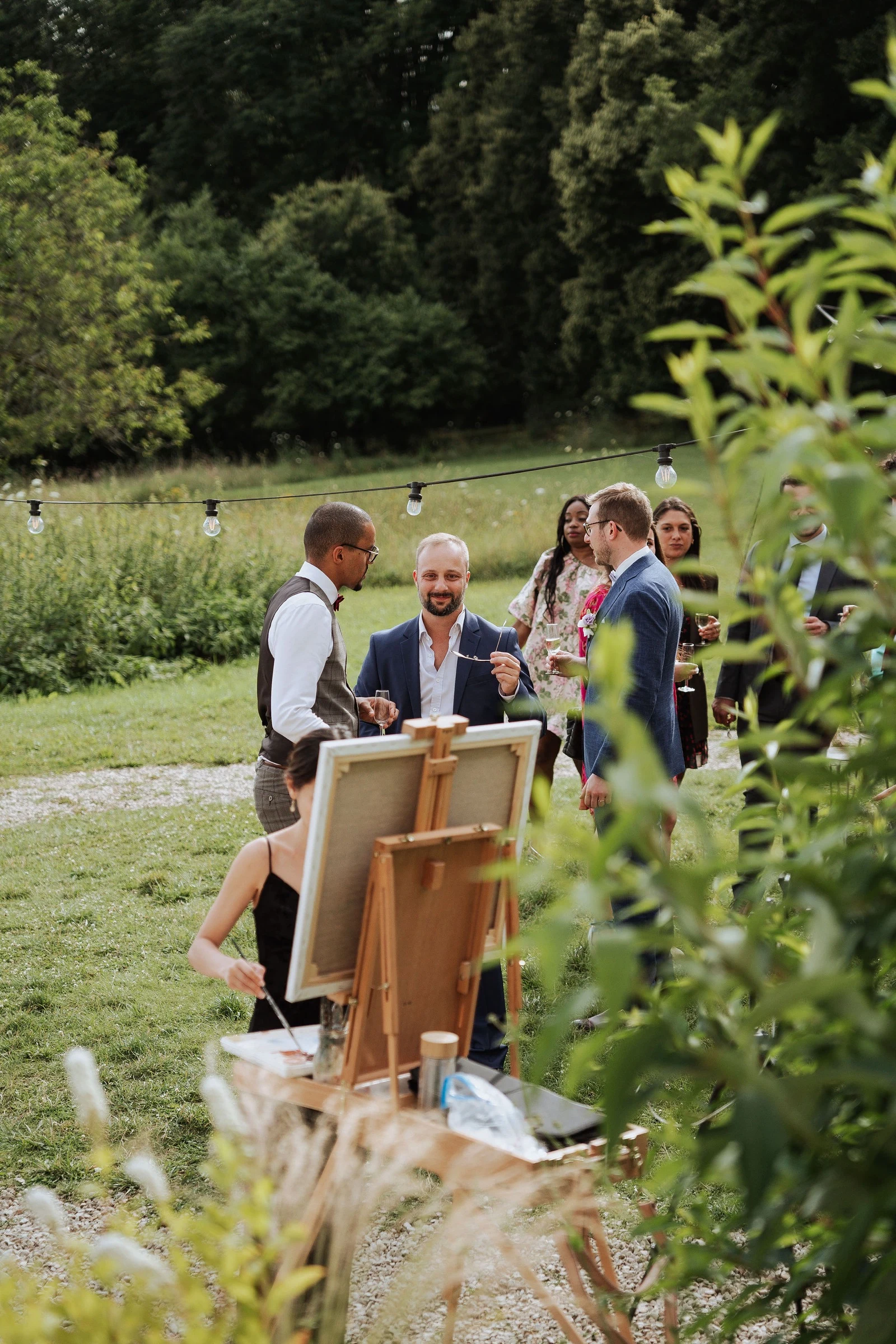Wide shot of guests gathered around Linh Dang’s easel during a wedding cocktail at Château du Feÿ. Photography by Kimmak Design.