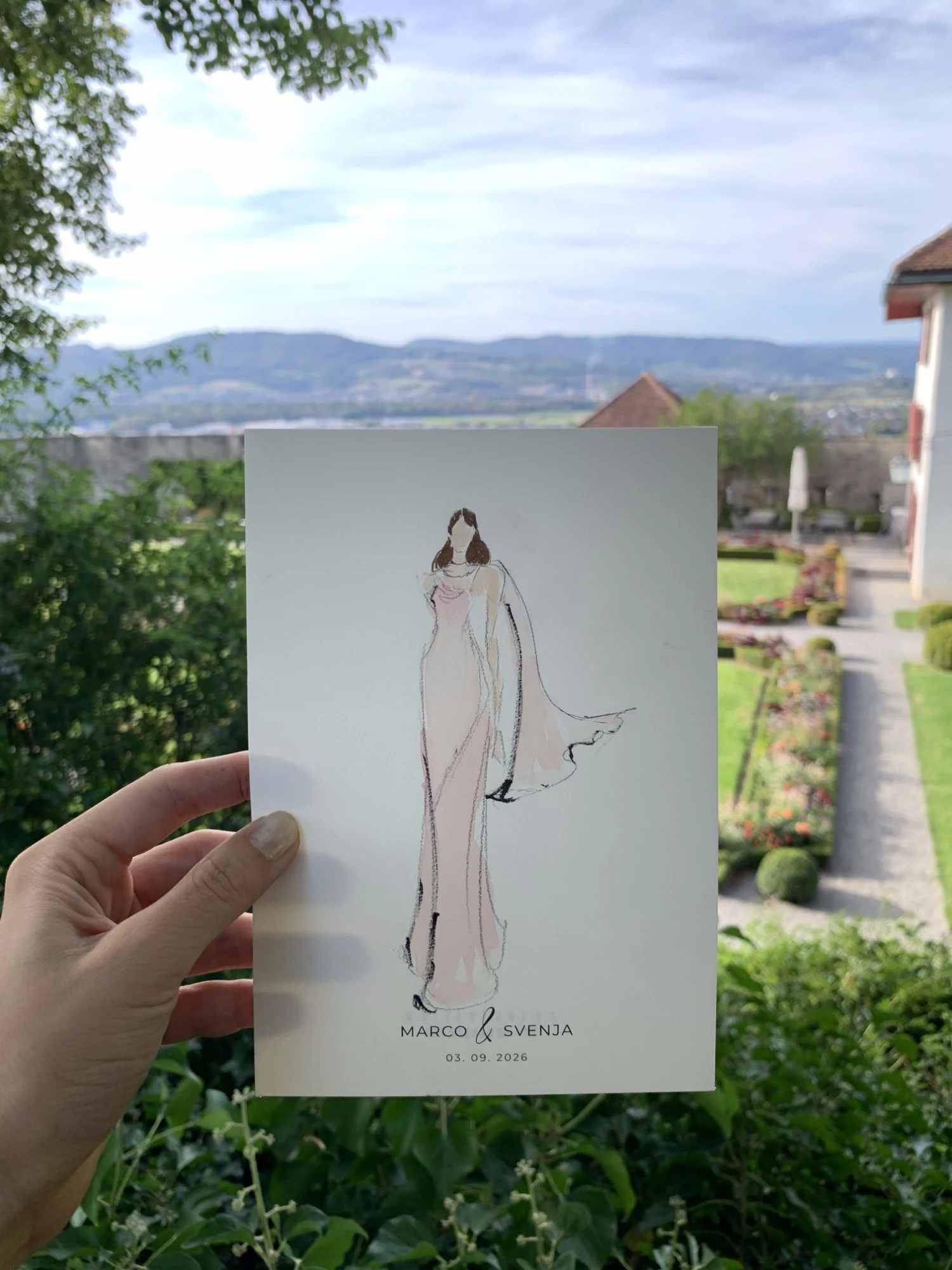 Live watercolor fashion sketch of a guest in a blush gown with a flowing cape, in the gardens of Schloss Lenzburg.