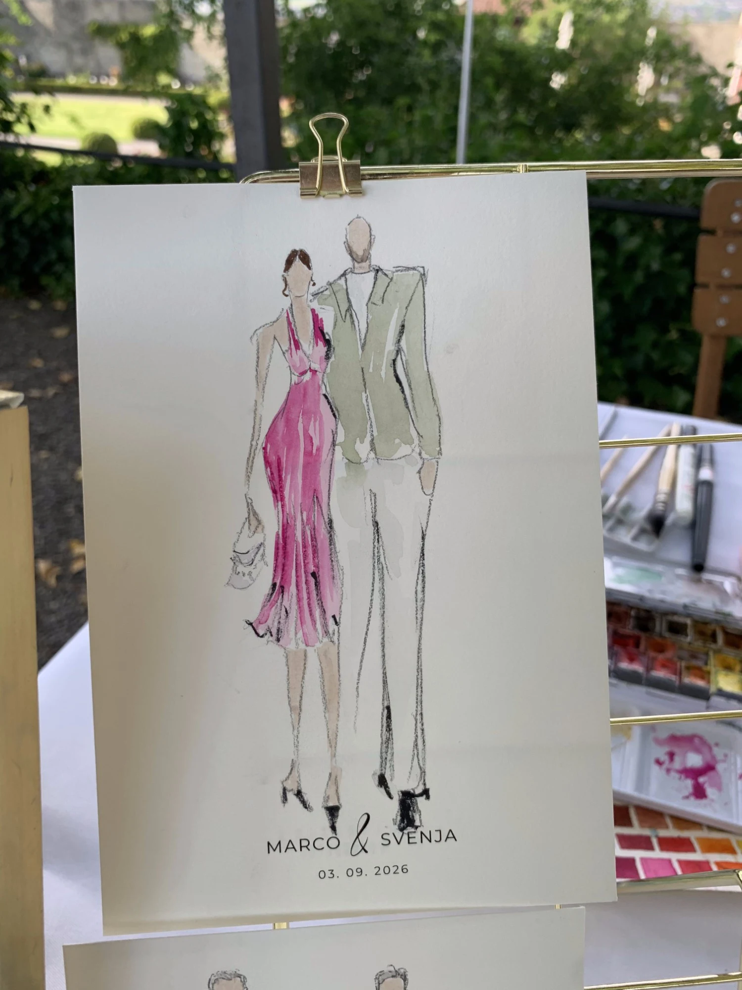 Live watercolor fashion sketch of a guest couple at Schloss Lenzburg: a pink halter dress and a sage suit.